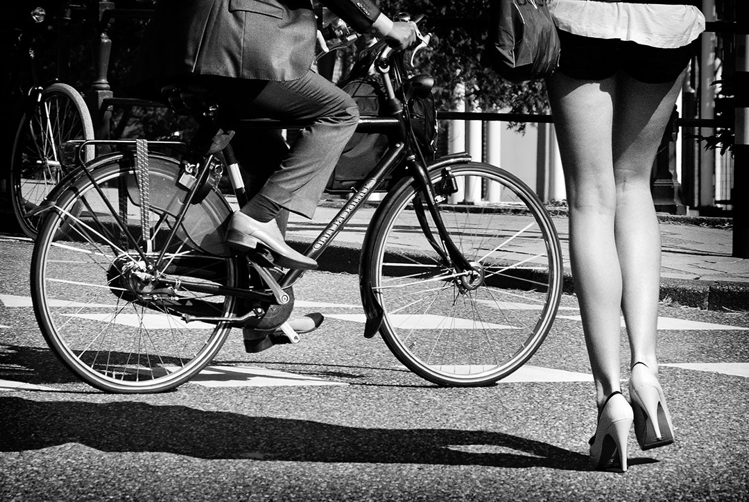 A bicycle passes beside the legs of a person wearing heels.